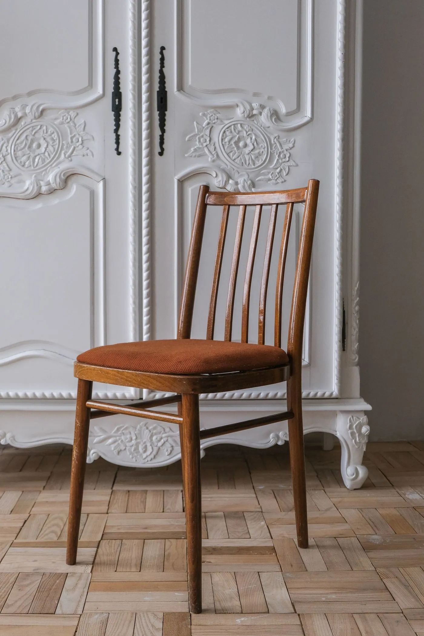 Wooden dining chair with a rust-coloured seat in front of a white cabinet