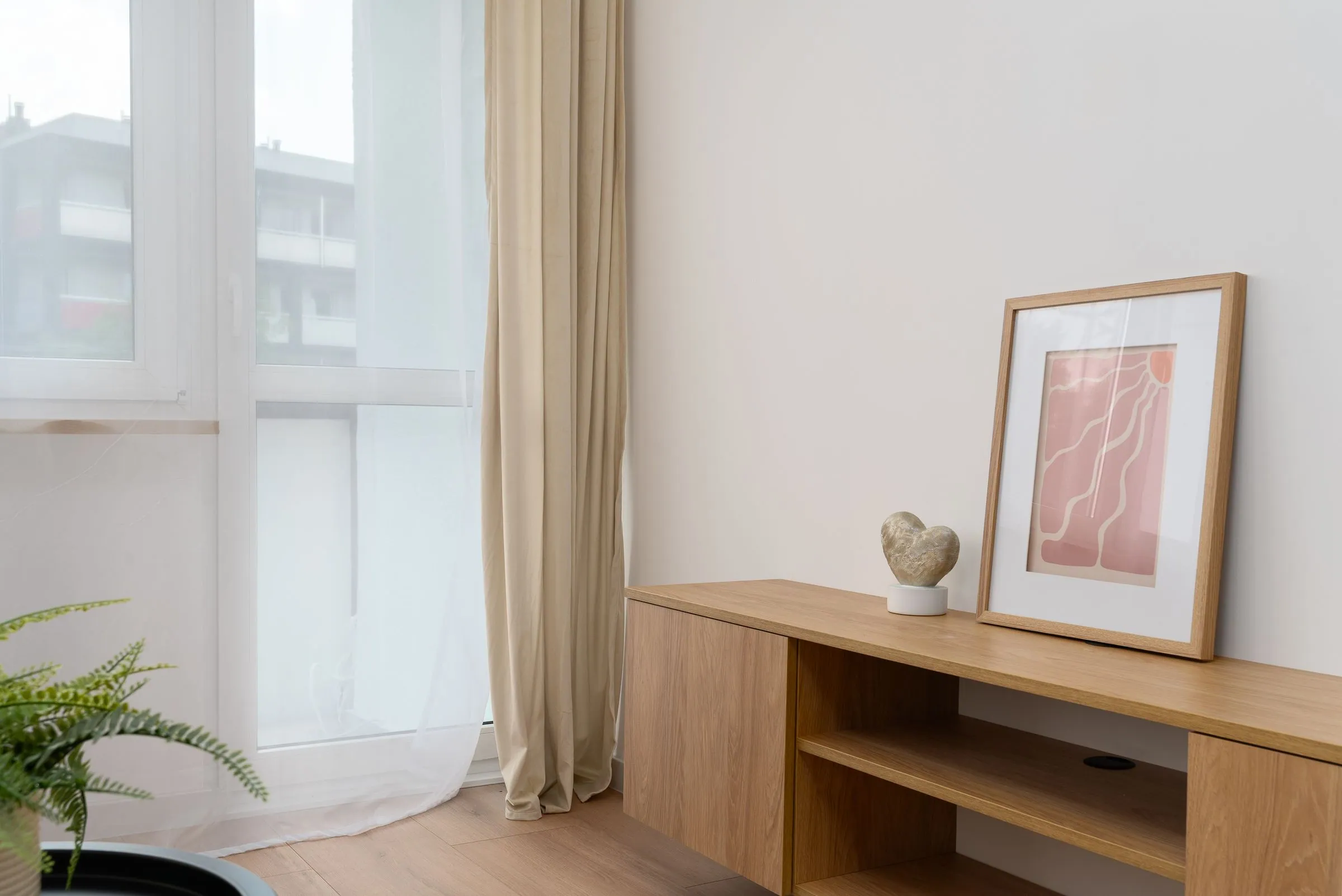 Low oak cabinet beneath a framed abstract print, with linen curtains and soft daylight