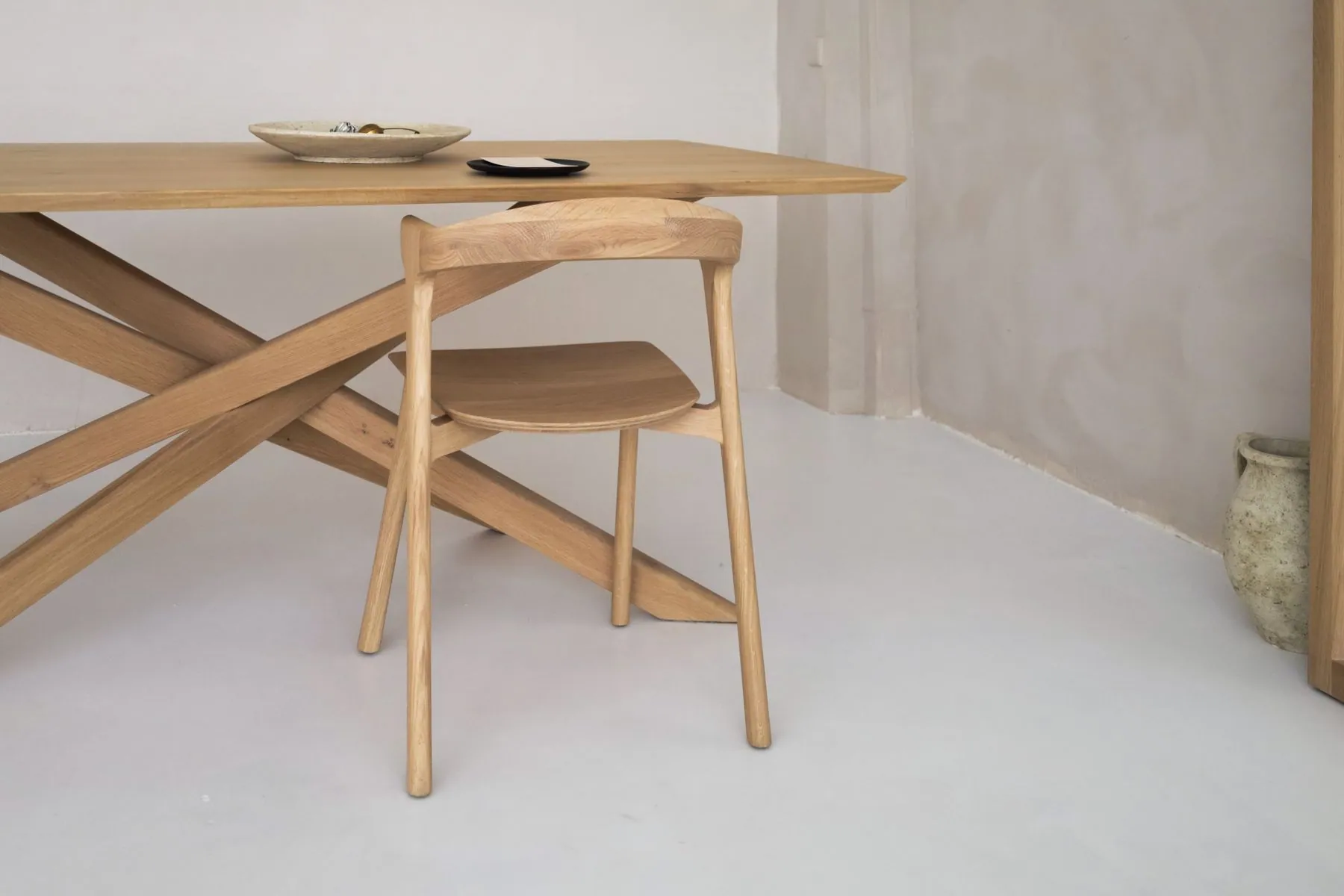 Sculptural oak dining table and chair against a plaster wall