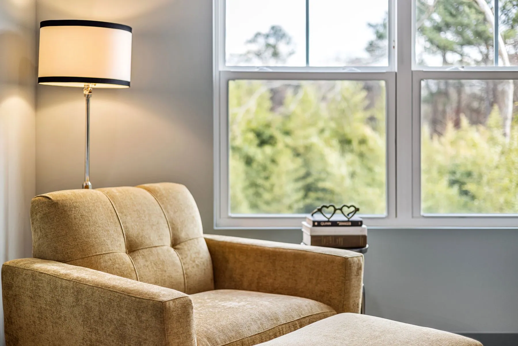 Upholstered armchair and footstool beside a floor lamp and a bright window
