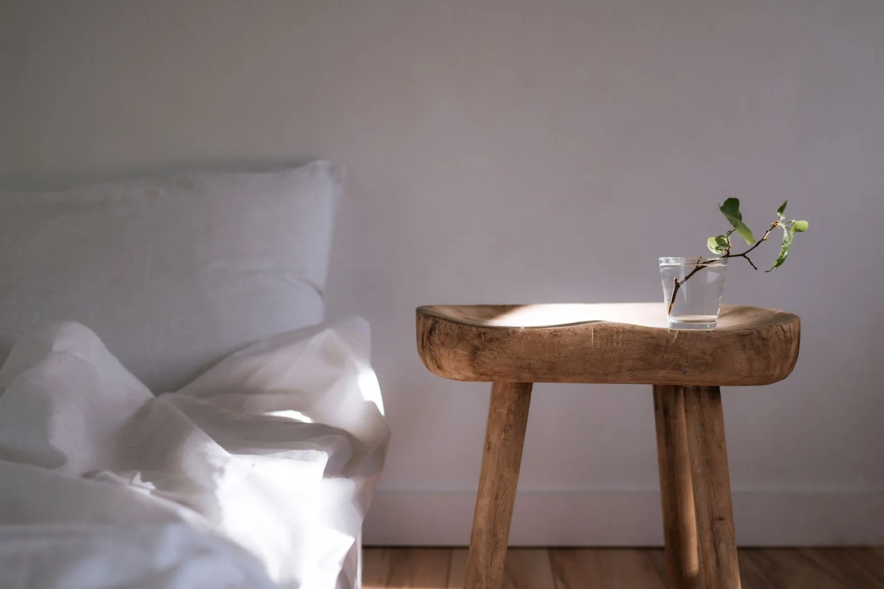 Rough-hewn wooden side table beside a bed dressed in white linen